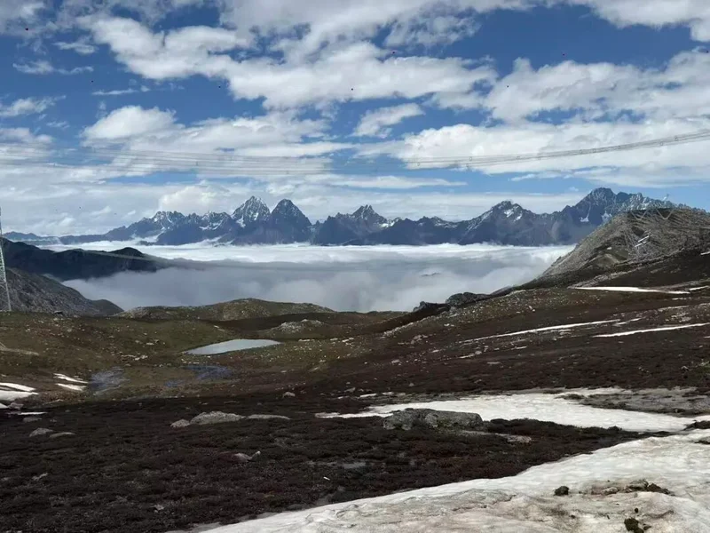 Panoramic view from a high-altitude ridge over jagged snow-capped peaks rising above a sea of clouds